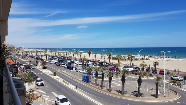 A coastal road with parked cars, palm trees, and a beach in the background. - THE PATIO APARTMENT FACING THE SEA (Canet-en-Roussillon)