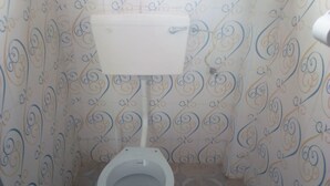 A small, narrow bathroom with a toilet and a wall-mounted sink. The walls are tiled with a decorative pattern. - Ideal Hotel (Kiriaini)