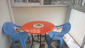 A small balcony with a tiled floor, a round table with a plate, and two blue plastic chairs. - Ideal Hotel (Kiriaini)