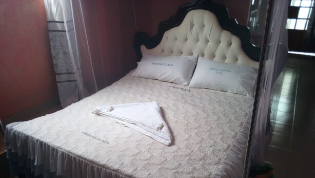 A neatly made bed with a white bedspread and pillows labeled 'GENNIS PLAZA'. - Ideal Hotel (Kiriaini)