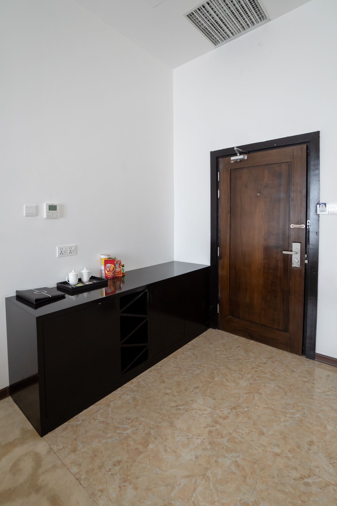 A room with a black desk, a wooden door, and a tiled floor.