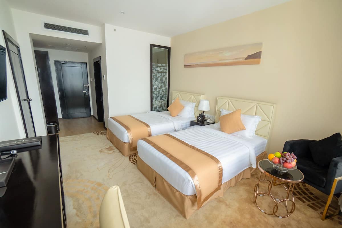 Habitación de hotel con dos camas, un escritorio, una silla y una mesita con fruta.