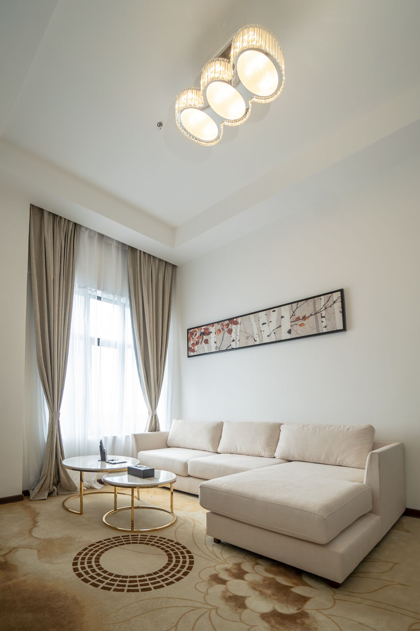 A modern living room with a beige sofa, a coffee table, and a large window with curtains.