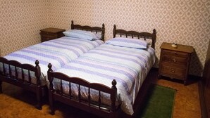 Una cama doble con una colcha a rayas, dos mesitas de noche, un aparador y un papel tapiz estampado.