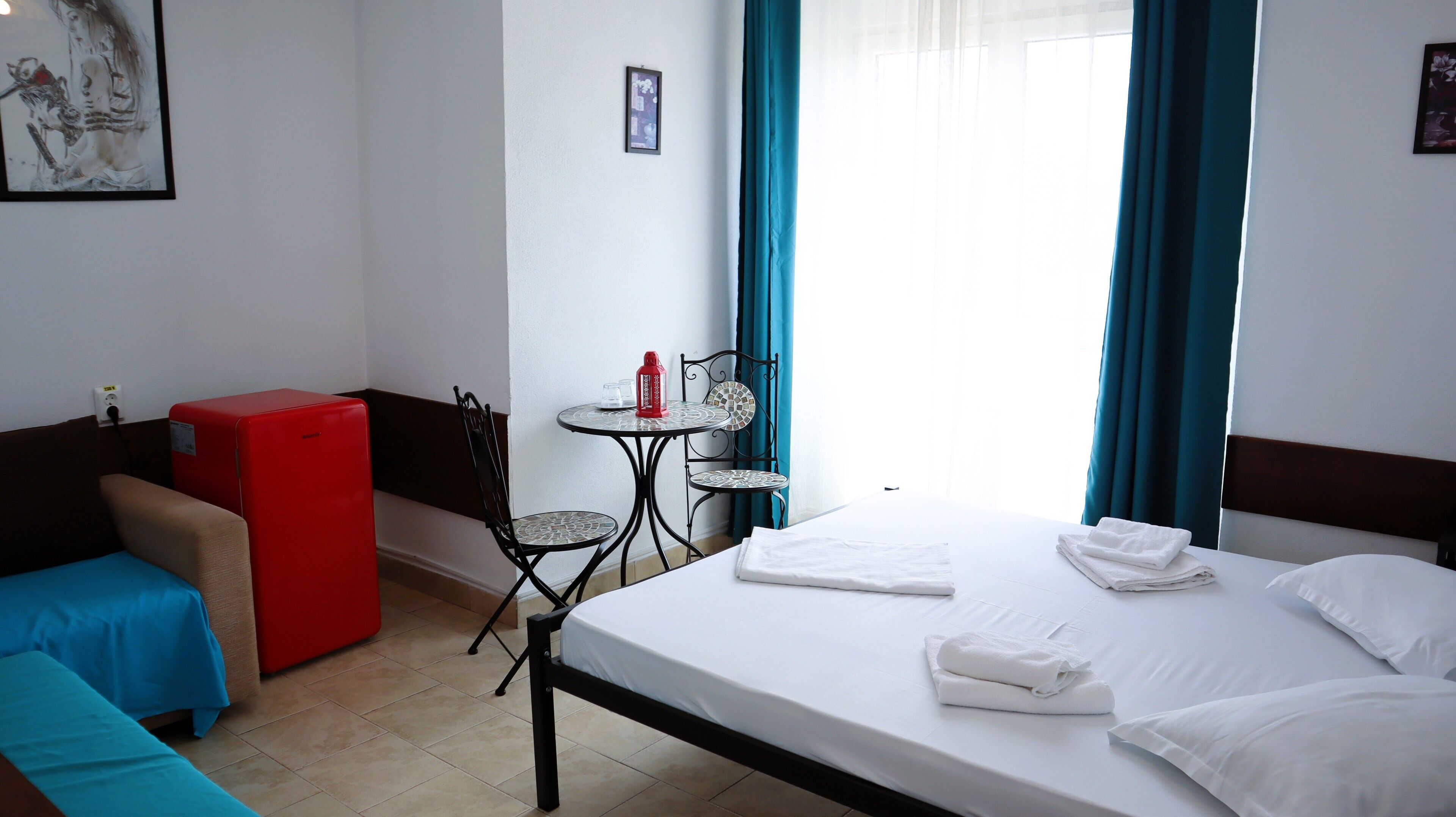 Una habitación de hotel con una cama, una mesita con sillas, un refrigerador rojo y un sofá azul.