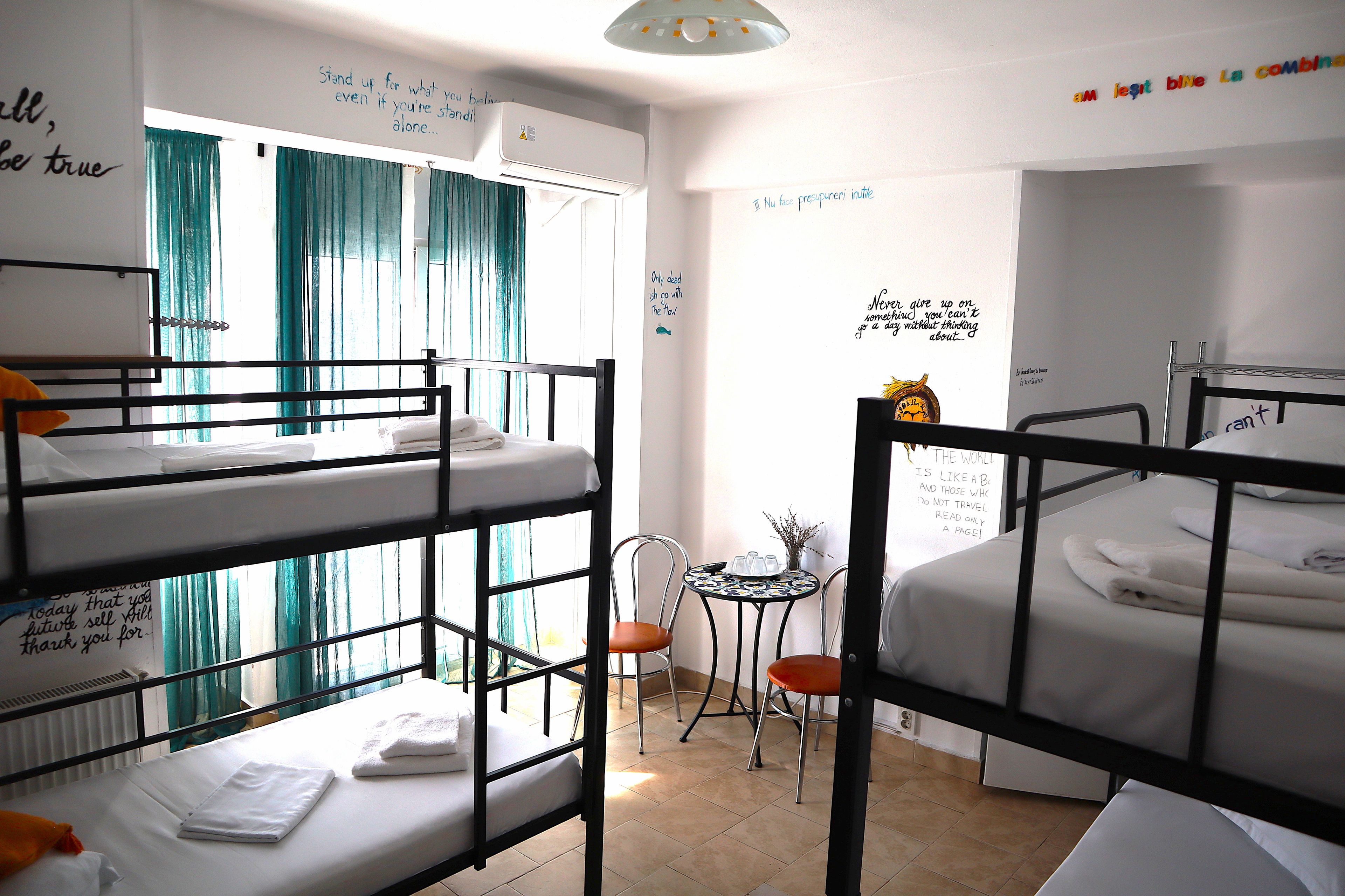 A dormitory room with bunk beds, a small table with chairs, and motivational wall art.