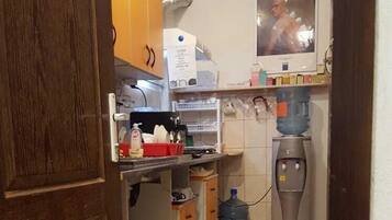 Cocina compacta con armarios de madera, cafetera, dispensador de agua y extintor.