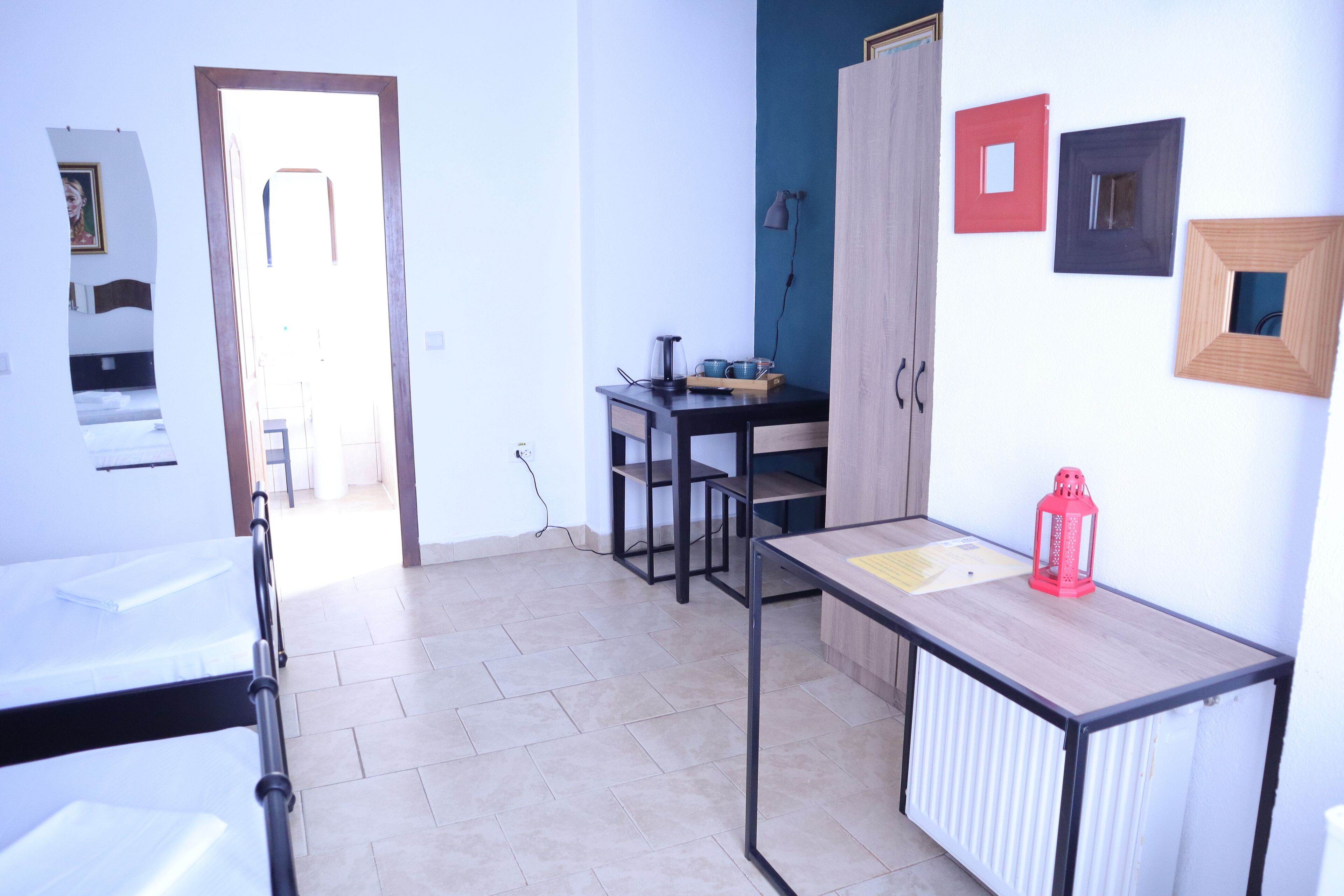 A room with a bed, a desk, and a radiator. There is a door leading to another room.