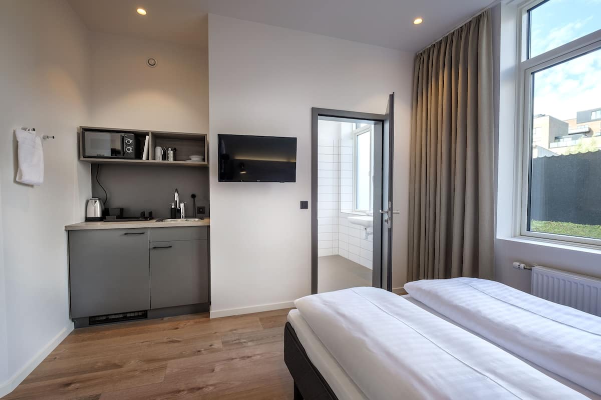 Ein modernes Schlafzimmer mit Bett, einer integrierten Küchenzeile, einem Fernseher und einem Fenster mit Vorhängen.