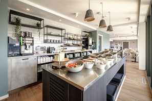 Una cocina moderna con electrodomésticos de acero inoxidable, una isla central con cuencos de comida y plantas colgantes.