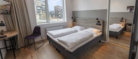 Moderni hotellihuone, jossa on suuri sänky, työpöytä, tuoli ja suuri ikkuna, josta avautuu näkymä kaupunkiin.