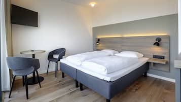 Ein modernes Hotelzimmer mit einem Bett, zwei Stühlen, einem kleinen Tisch und einem wandmontierten Fernseher.