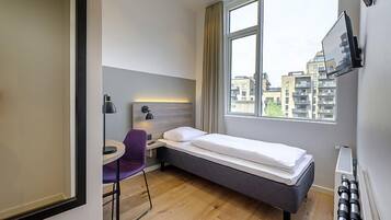 Habitación de hotel pequeña con una cama individual, un escritorio, una silla y ventana con vista a la ciudad.