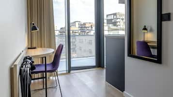 Una habitación de hotel moderna con un ventanal grande, una mesita pequeña, una silla morada y un espejo en la pared.