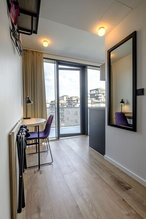 Una habitación de hotel moderna con un ventanal grande, una mesita pequeña, una silla morada y un espejo en la pared.