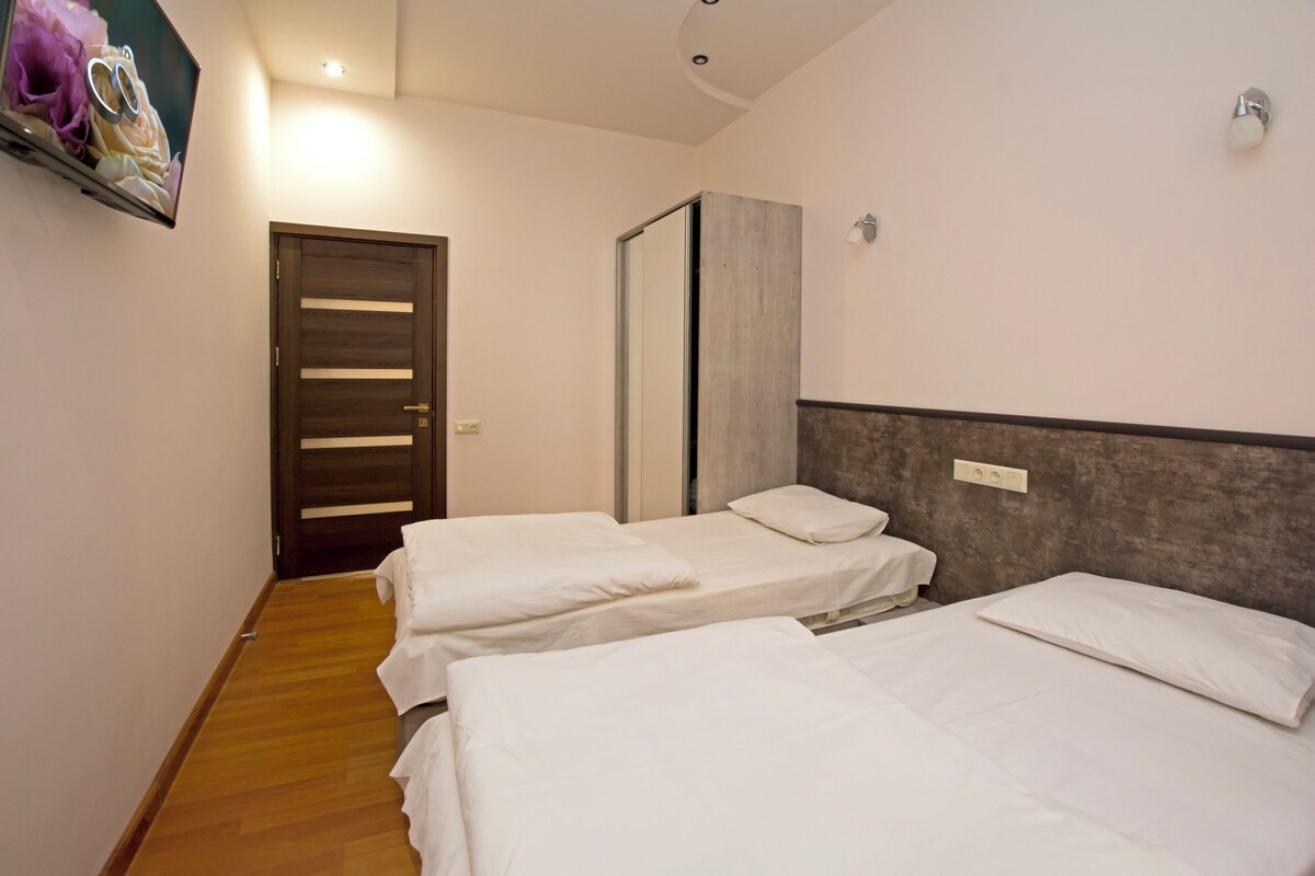 A hotel room with two single beds, a wooden floor, a door with a mirror, and a wall-mounted TV.
