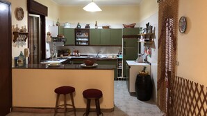 Cuina amb armaris verds, una illa central amb tamborets, un refrigerador i diversos objectes de cuina als taulells.