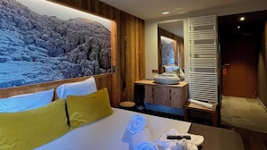A modern hotel room with a large bed, wooden headboard, and a view of a rocky landscape through a large window.