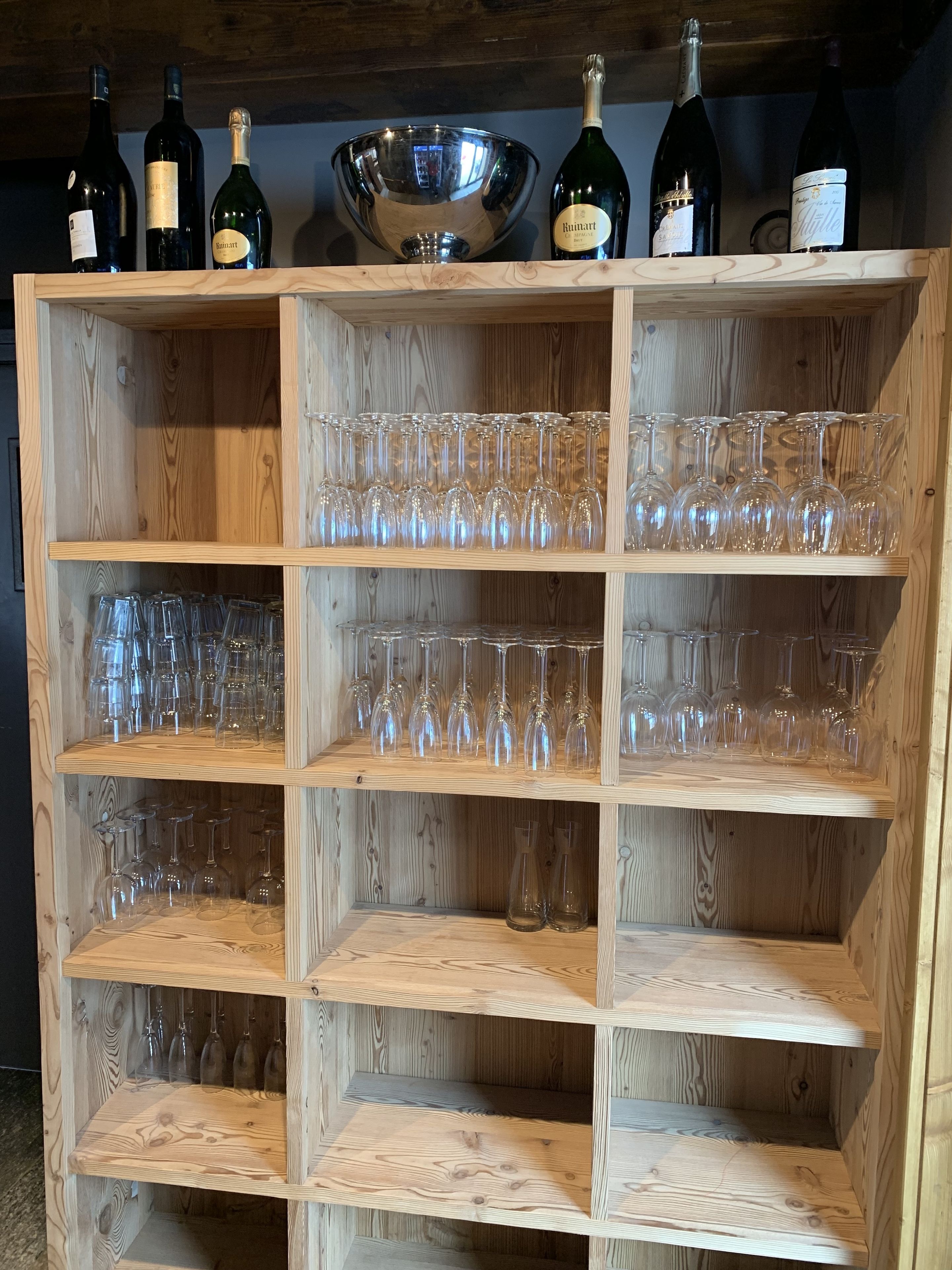 A wooden wine rack with multiple shelves holding wine bottles and glasses.