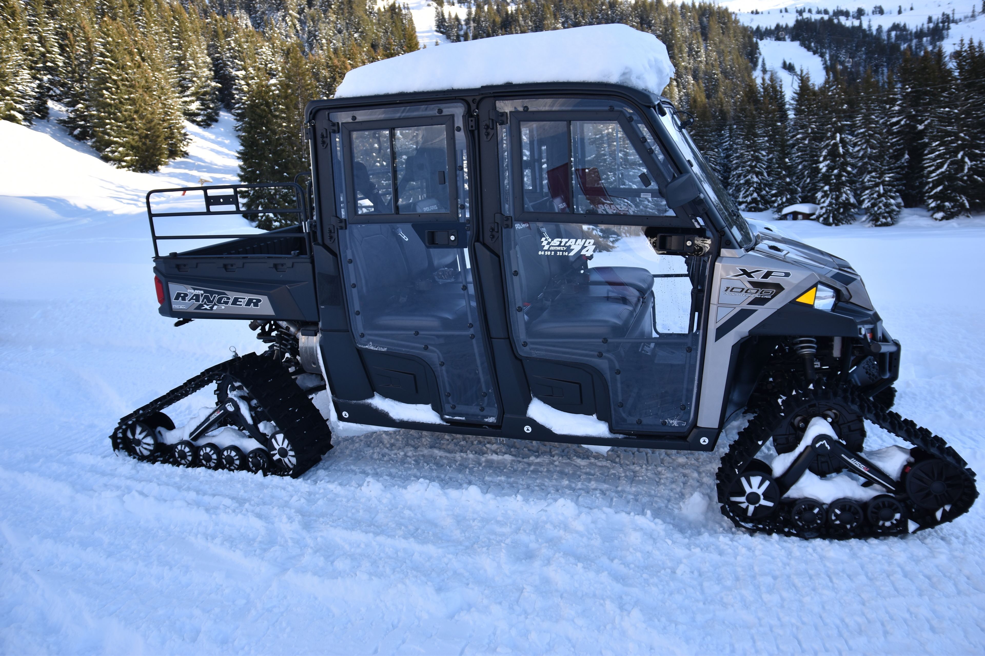 Un vehículo para nieve con logotipo "Ranger" e identificación "XP", equipado con orugas, estacionado sobre nieve.
