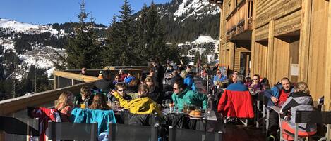 A wooden building with a terrace dining area overlooking a snowy mountain landscape.