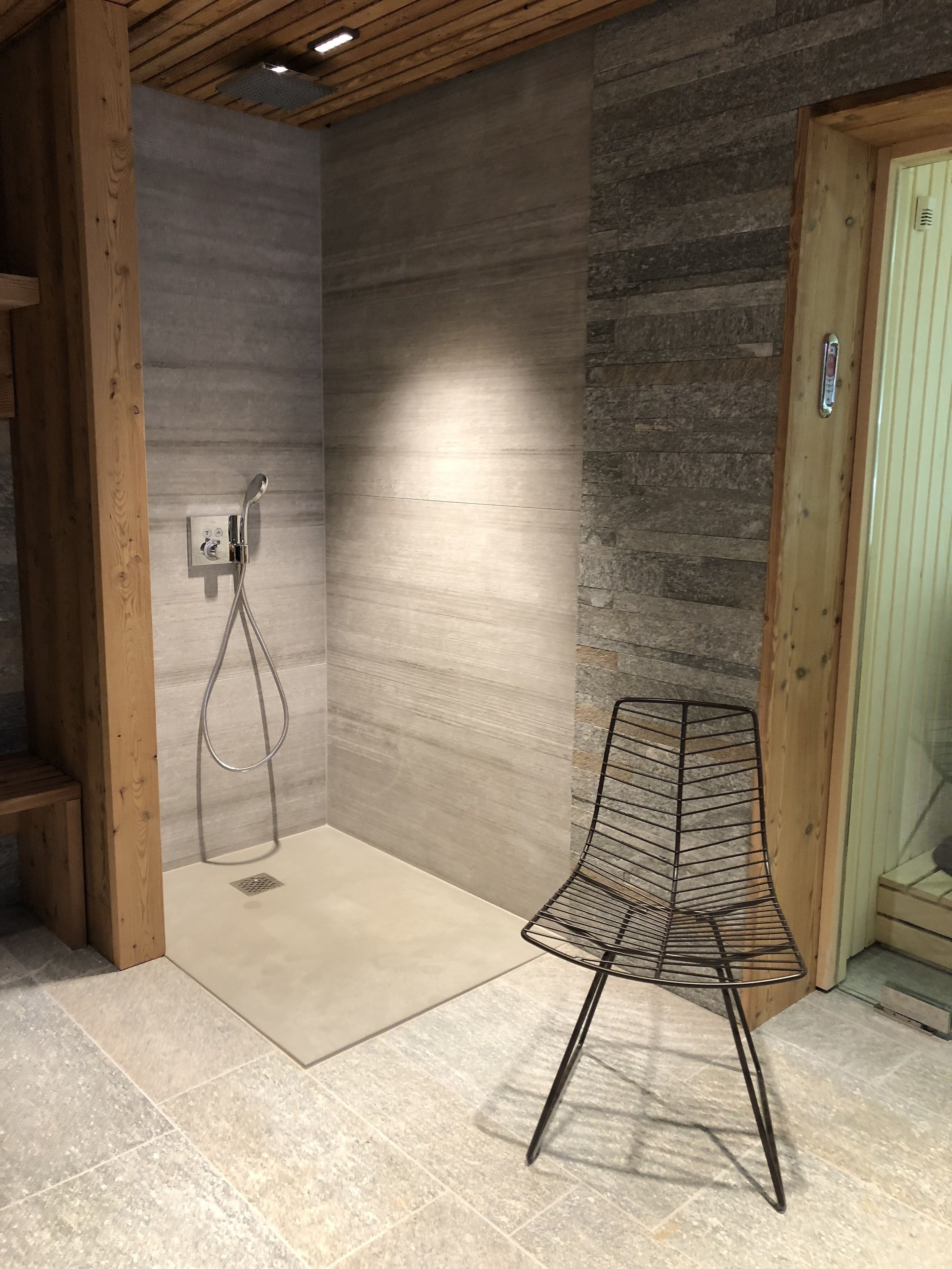 A shower area with a wooden bench, a metal chair, and a stone wall.