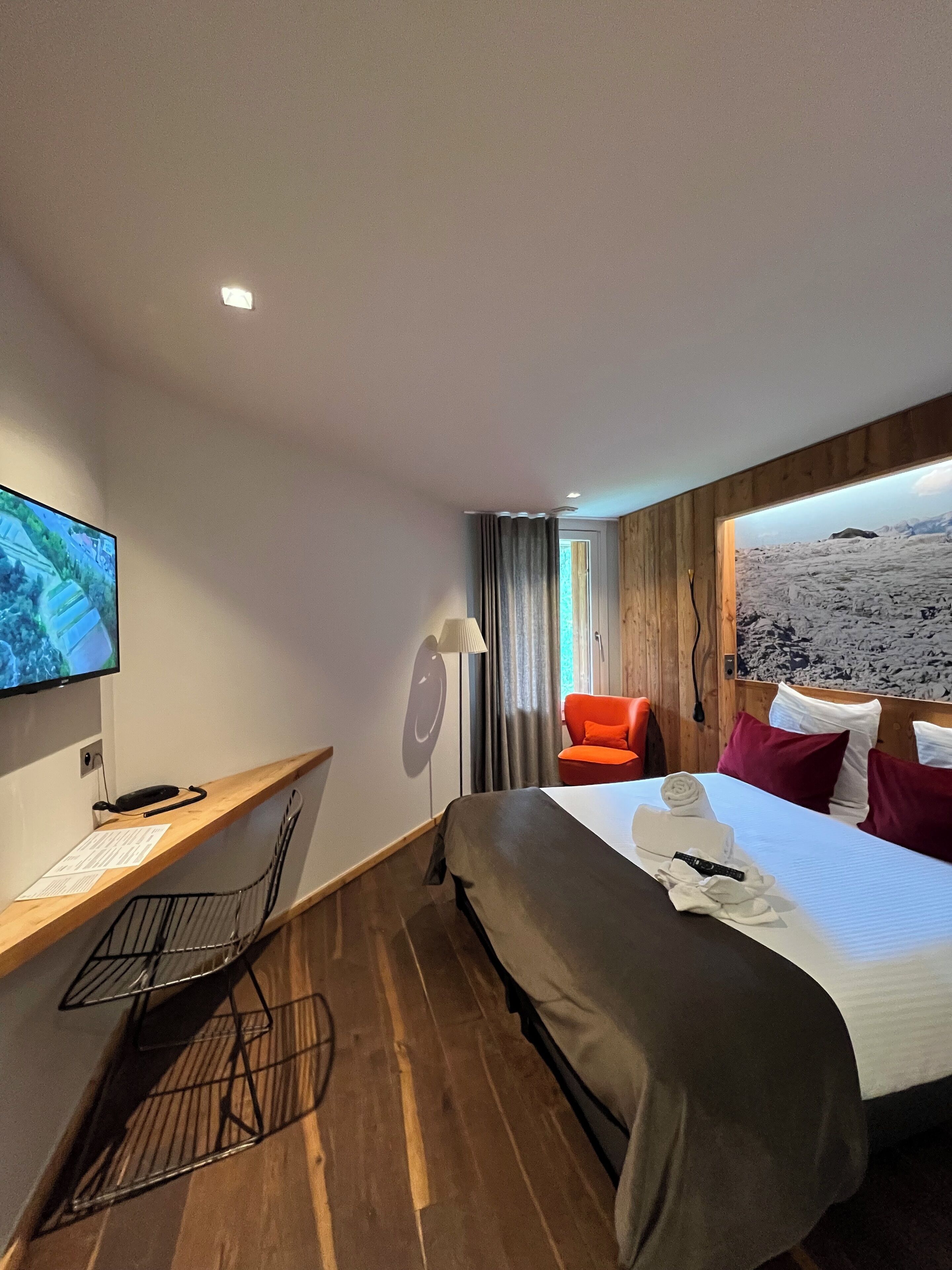 Habitación de hotel con una cama, un escritorio con computadora, una silla y un televisor en la pared.