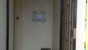 Une entrée étroite avec un portail en métal, une petite table ornée d’un objet décoratif et une enseigne fixée au mur.