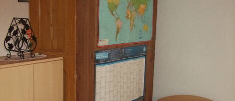 Una habitación pequeña con cama individual, cabecera de madera, un mapa mundial y un calendario en la pared.