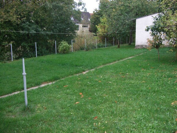 A grassy outdoor area with a path, trees, and a white building in the background. - Gästehaus Kissel (Niederkirchen)