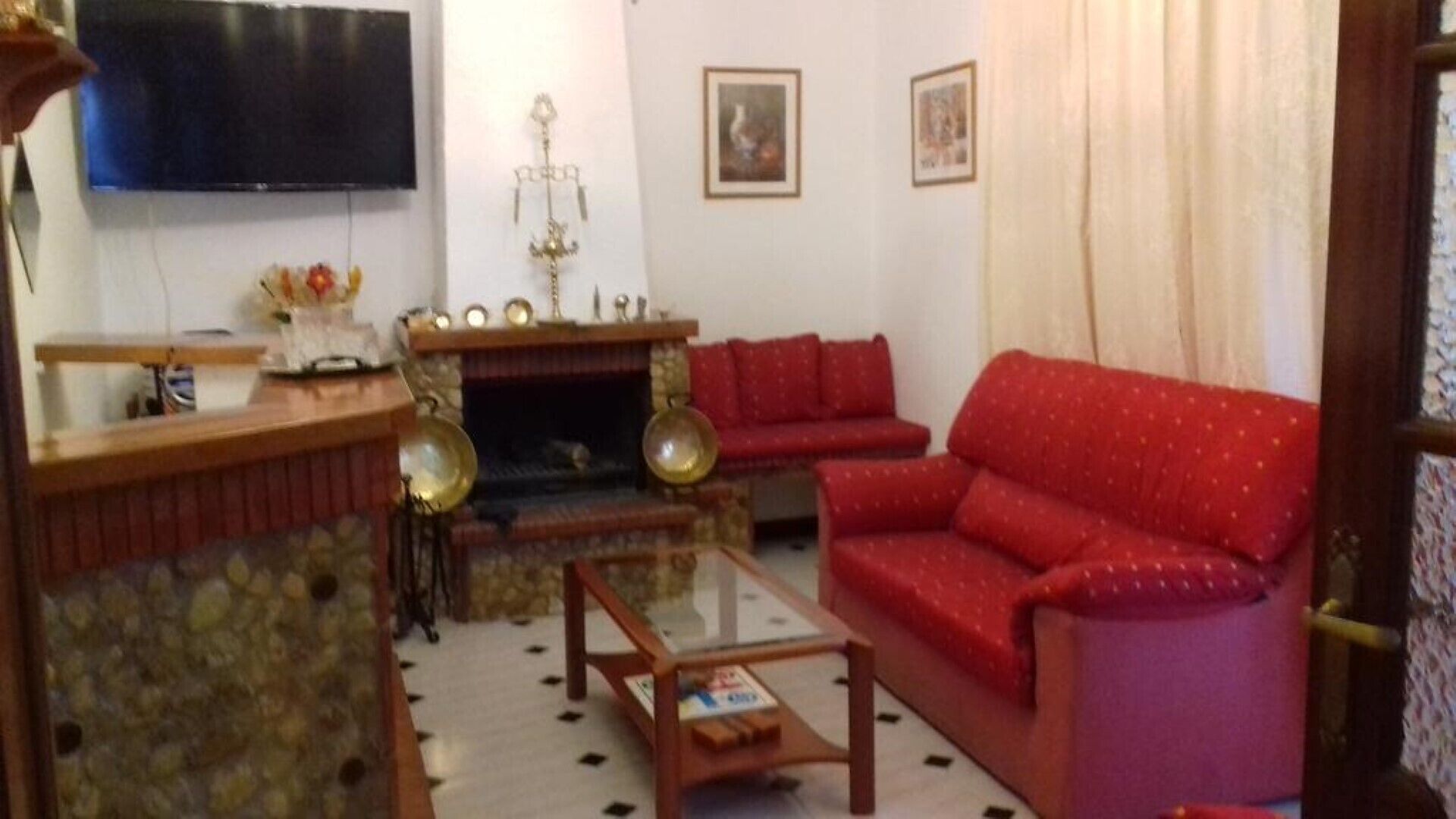 Un salon avec un canapé rouge, une cheminée, un téléviseur et un mur en pierre.