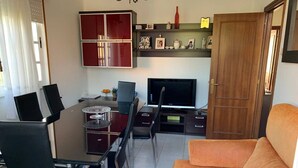 Uma sala de estar com área de jantar, televisão e sofá.