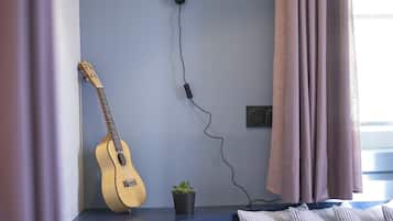 A room with a blue sofa, a guitar leaning against the wall, a small plant, and a floor lamp.