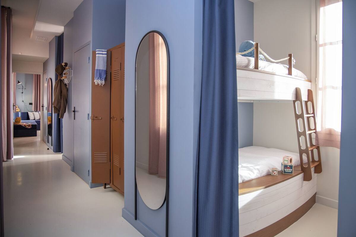 Een stapelbed met een ladder, een spiegel en een kledingkast in een kamer met blauwe wanden en een deur naar een andere kamer.