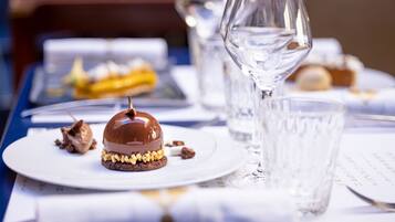 A dessert plate with a chocolate dome and nuts, a glass of water, and a dessert tray in the background.