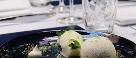 A dessert plate with two white meringues and a scoop of ice cream, garnished with mint leaves and edible flowers, on a dark plate.