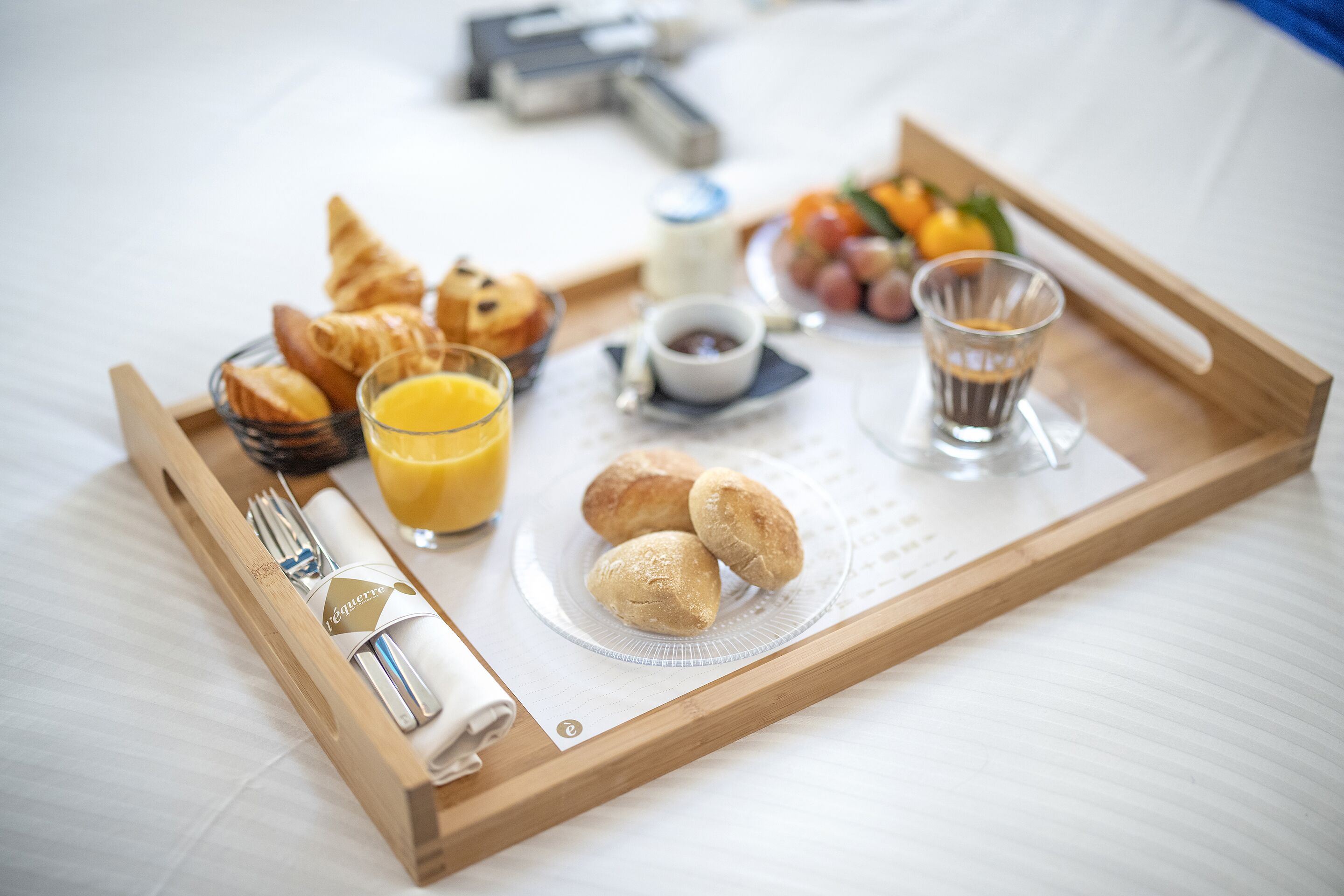 Un plateau de petit-déjeuner avec des croissants, du jus, du café et un petit pot de confiture, posé sur le lit.