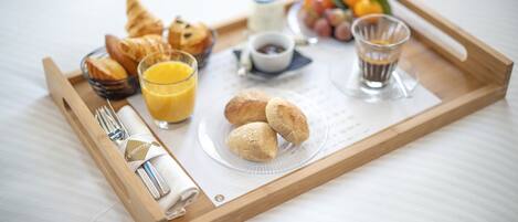 Un plateau de petit-déjeuner avec des croissants, du jus, du café et un petit pot de confiture, posé sur le lit.