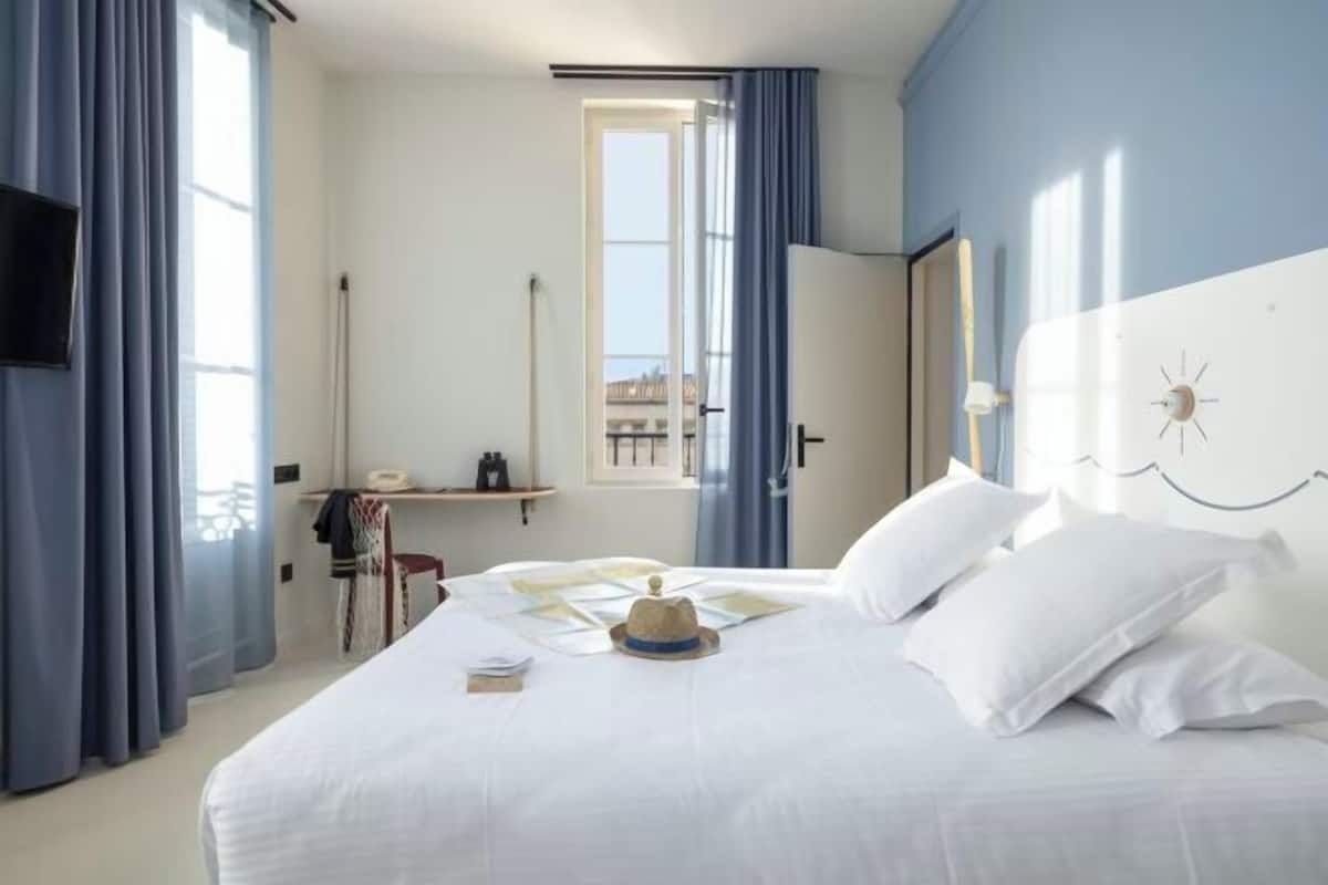 Een hotelkamer met een bed, een bureau, een stoel, een televisie en een raam met gordijnen.