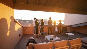 Eine Dachterrasse mit Blick auf die Stadt, Holzmöbel und ein Tisch mit Hut und Sonnenbrille.