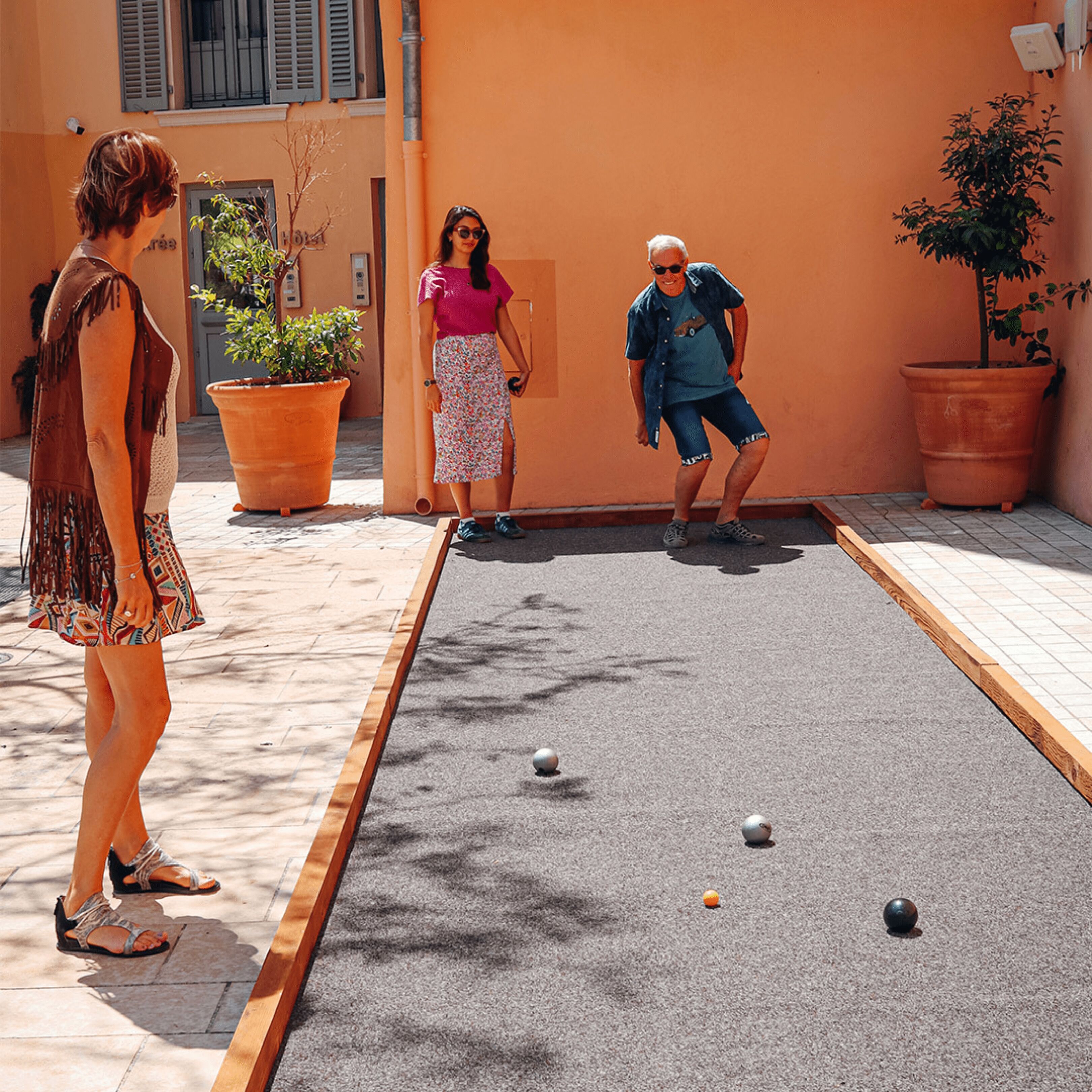 A courtyard with a shuffleboard table, potted plants, and a building with shutters.