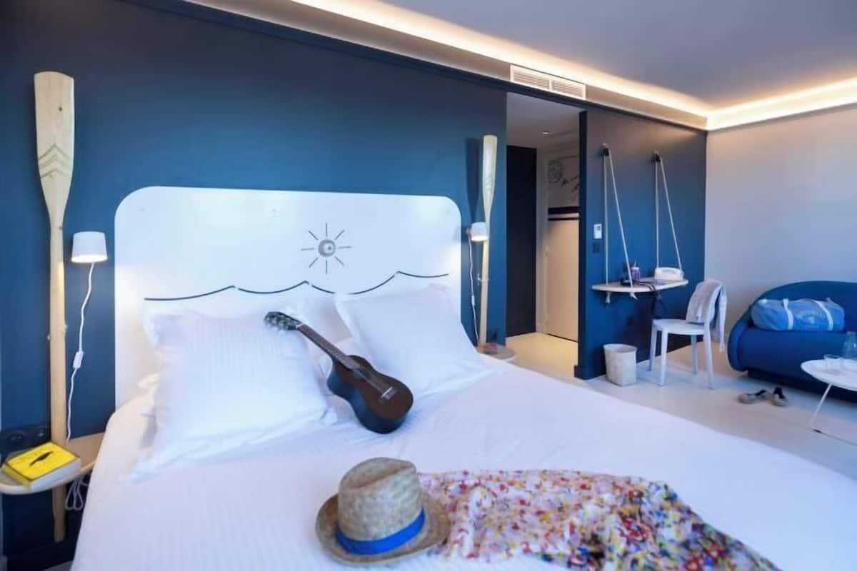 Een hotelkamer met een bed, een gitaar, een hoed en een stoel.