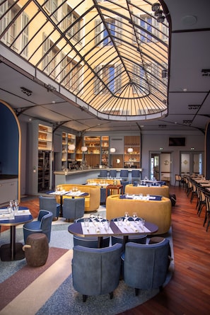 Un restaurante espacioso con un alto techo y una cúpula de cristal central, que cuenta con varias zonas de estar con mesas y sillas.