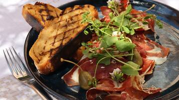 A plate of food with grilled bread, prosciutto, and greens on a table with a white tablecloth.