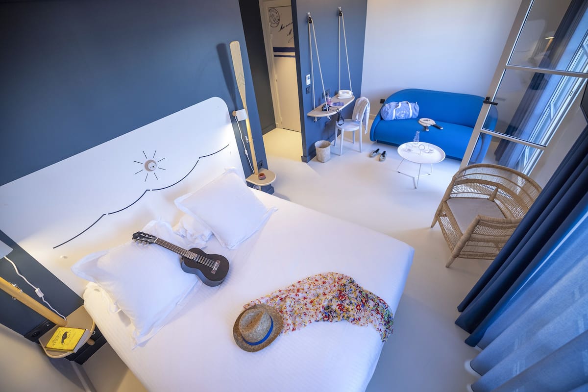 Een hotelkamer met een bed, een gitaar, een hoed en een stoel.