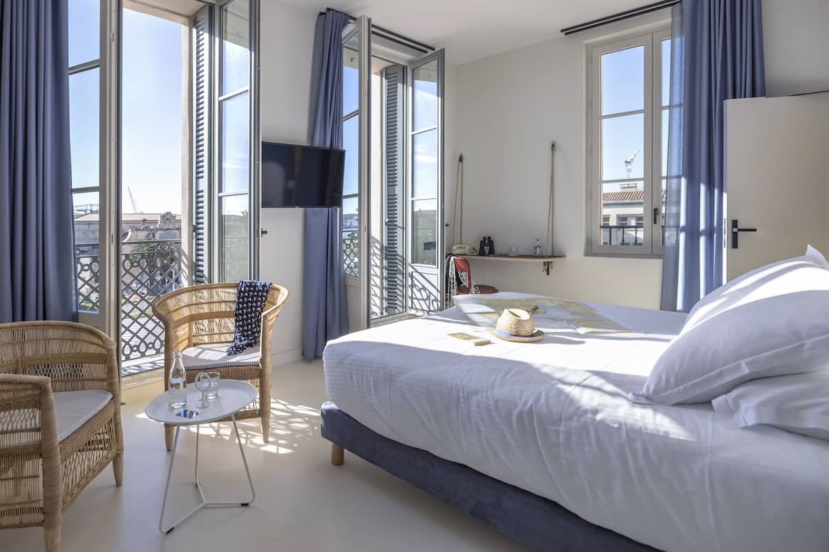 Een hotelkamer met een bed, een rieten stoel, een tafeltje en een balkon met uitzicht.