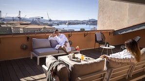 A rooftop terrace with a view of a harbor, featuring a sofa, a small table with drinks, and a chair. - Hôtel L'Eautel Toulon Port (Toulon)
