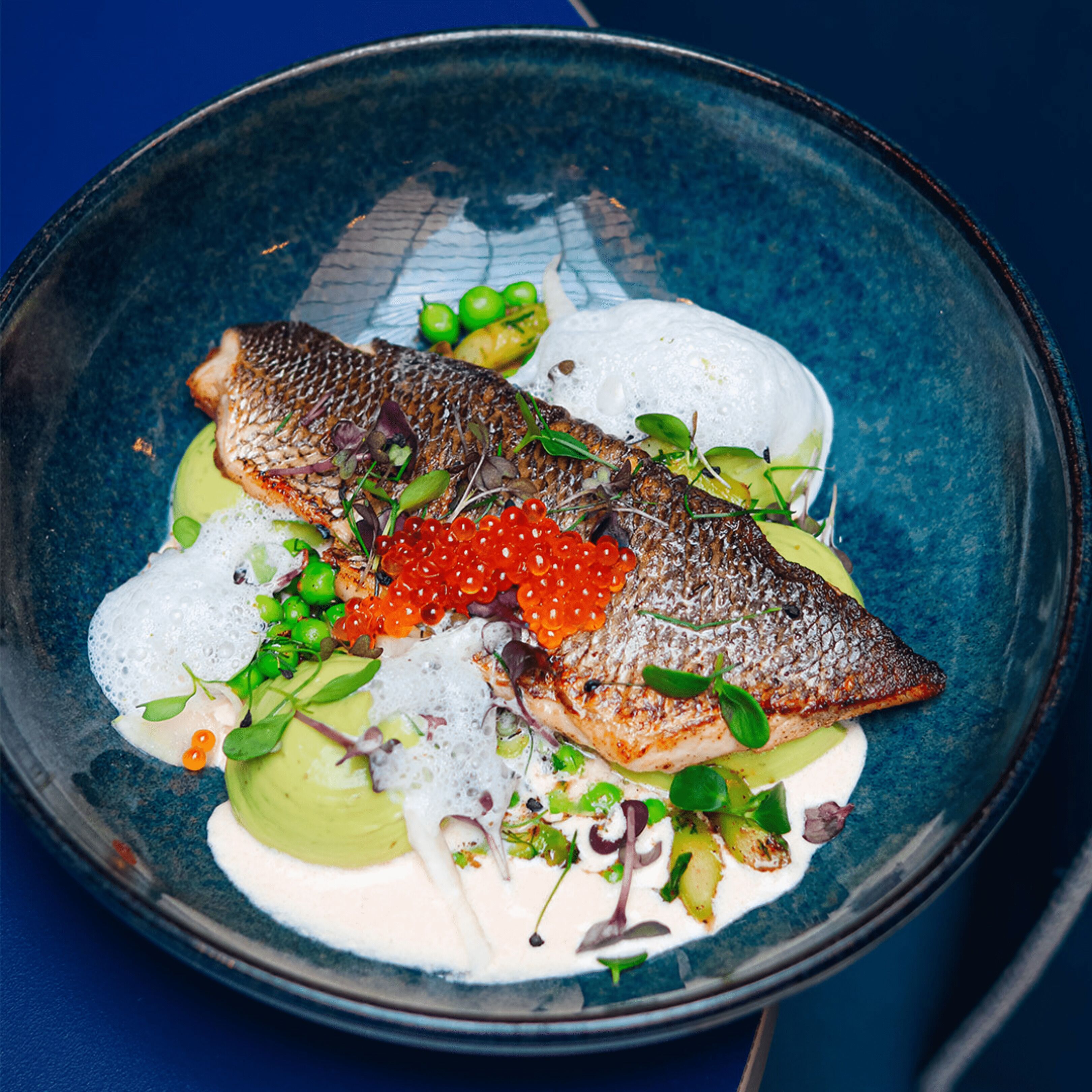 Un piatto con pesce, caviale e verdure su un piatto blu.