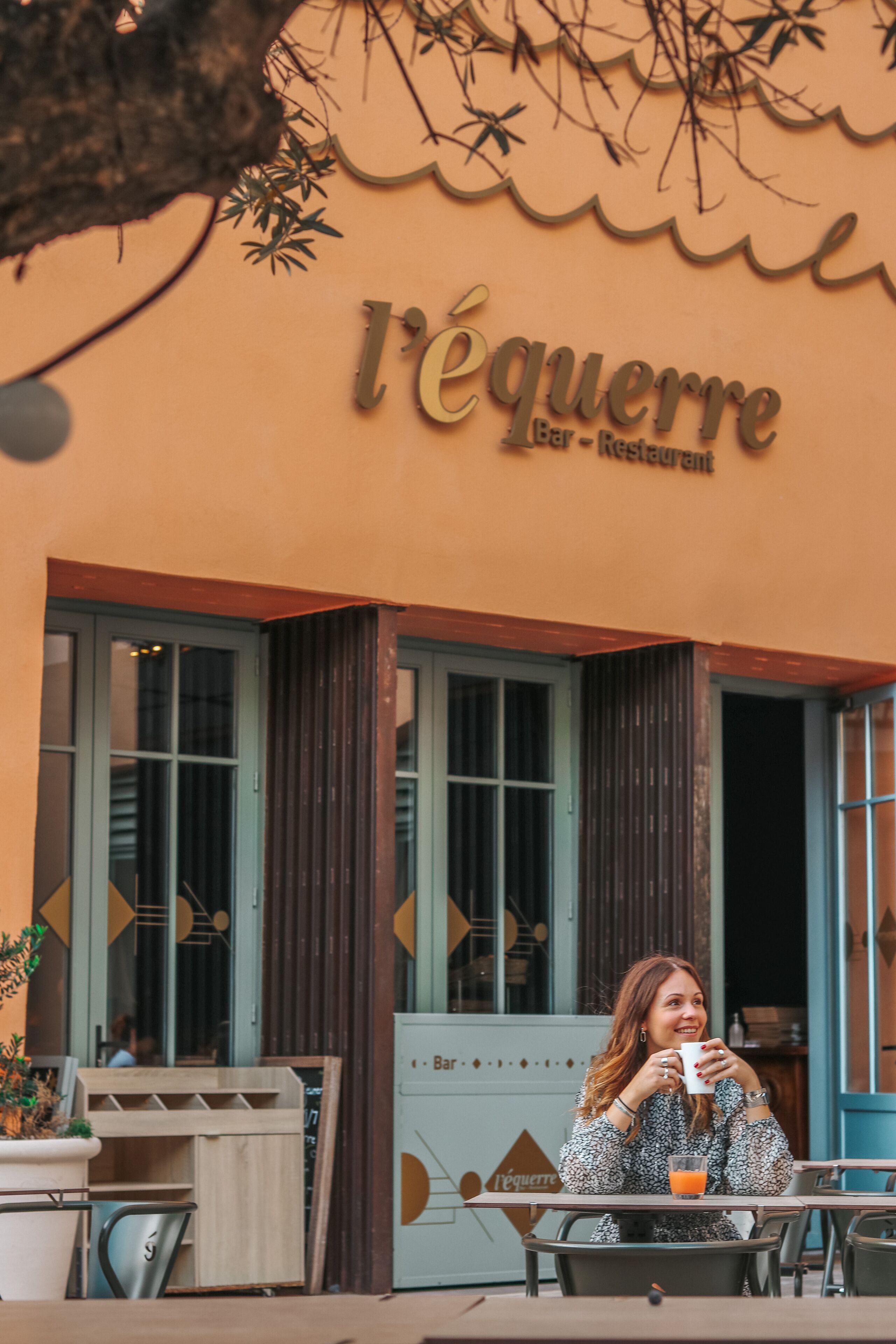 Una cafetería llamada 'l'équerre' con terraza y fachada de madera rústica.