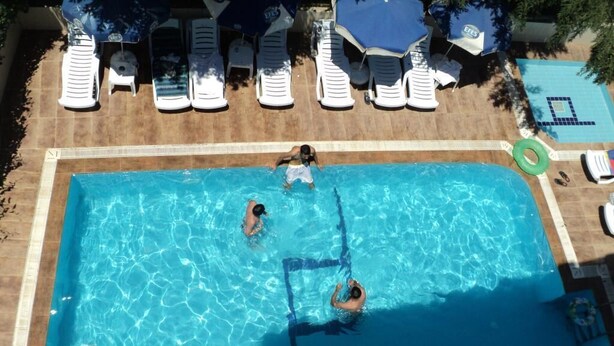 Una piscina rectangular con agua azul cristalina, rodeada de sillas reclinables y sombrillas blancas.